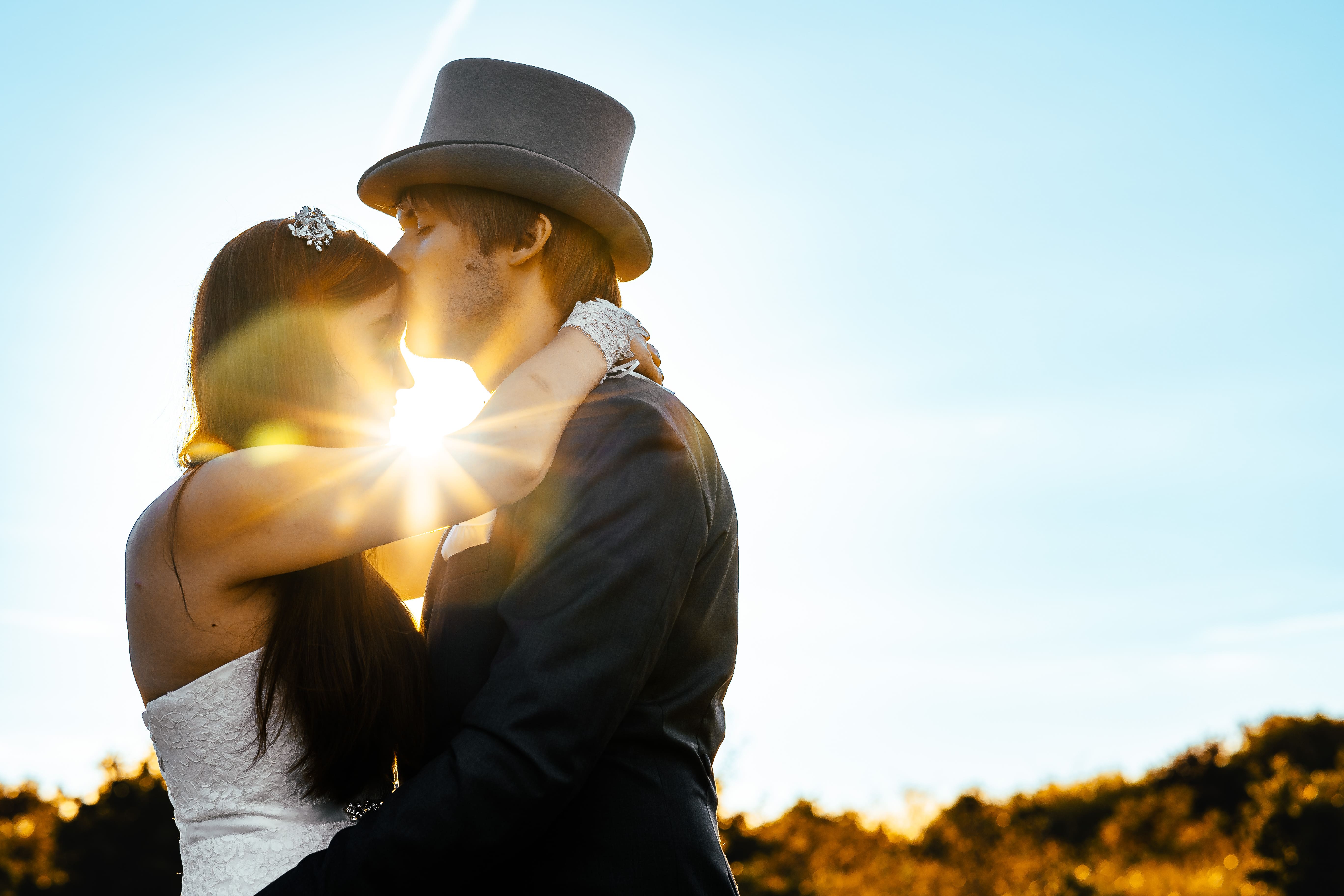 Braut bekommt von Bräutigam einen Kuss auf die Stirn im Sonnenlicht